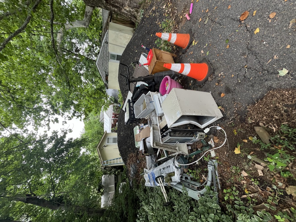 Before junk removal in Woodbridge, NJ: a driveway piled with old appliances, bins and debris